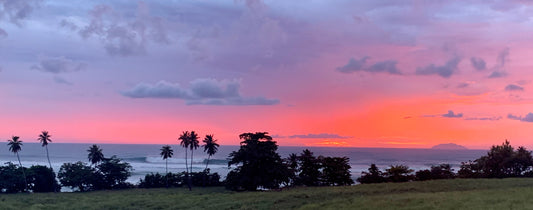 A breathtaking sunset over Tres Palmas Reserve, with rolling waves breaking. The warm colors of the sky blend together, creating a stunning display of oranges, pinks, and purples.