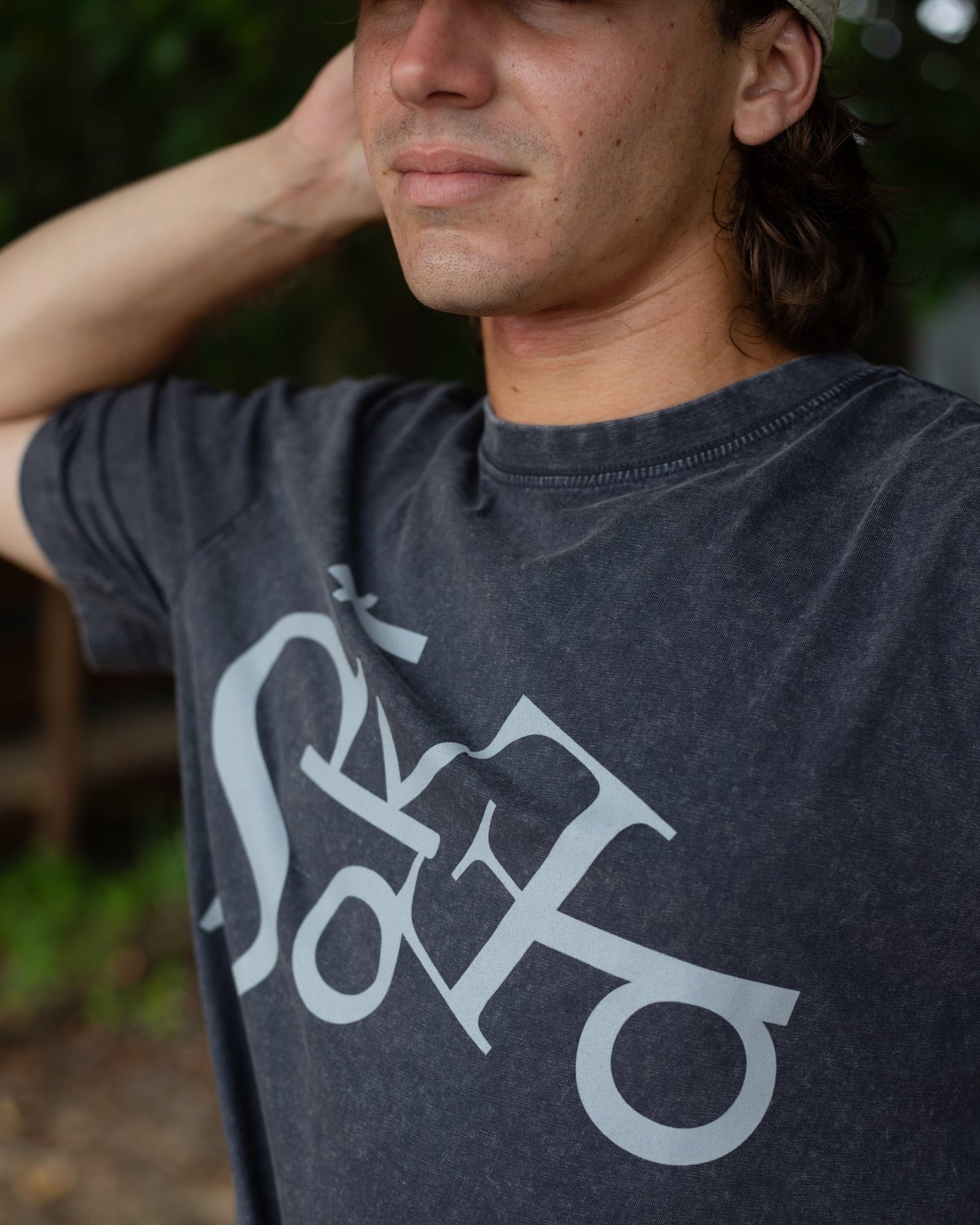 Person wearing a dark gray t-shirt with a logo, standing outdoors.